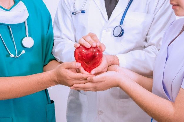 doctores y enfermera tomando un corazón rojo referenciando al cuidado del paciente
