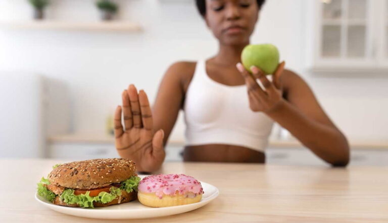 mujer evitando comer una hamburguesa y dona a cambio de una manzana